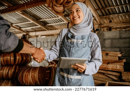 beautiful young muslim woman shake hand with customer in her woven bamboo product workshop