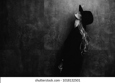 Linda jovem e misteriosa menina loira em chapéu preto e jaqueta preta no fundo cinza. Os olhos estão cobertos com um chapéu. Manicure - unhas vermelhas longas, esmalte de unhas. Moda, beleza.