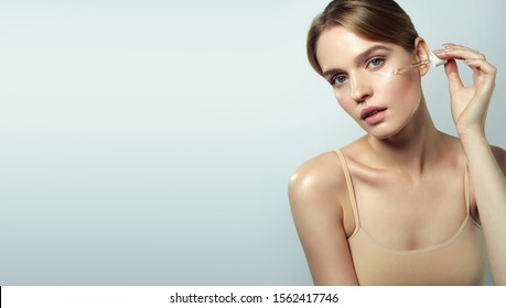 A beautiful young natural girl without makeup applies a serum to a face with a pipette. - Shutterstock ID 1562417746