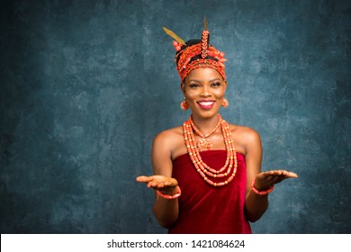 beautiful young nigerian woman wearing edo bridal attire stretching forward her open palms and smiling