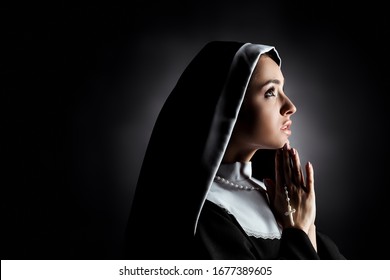 beautiful young nun looking up while praying with cross on grey