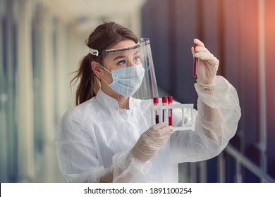 beautiful young nurse in protective mask and face shield and uniform examines blood samples in test tube for coronavirus infection. covid19