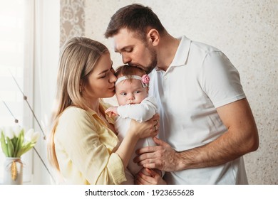 Beautiful Young Parents Kiss Their Baby Girl In A Bright Room