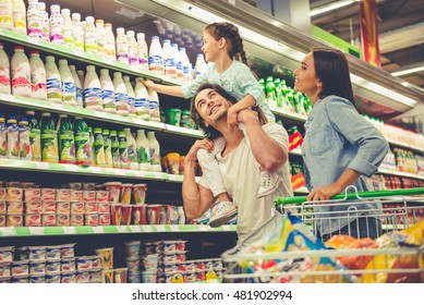 Beautiful young parents and their cute little daughter are smiling while choosing food in the supermarket. Girl is sitting on her dad's shoulders - Powered by Shutterstock