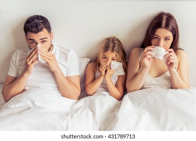 Beautiful young parents and their daughter are having common cold, wiping noses and looking at camera while lying on bed