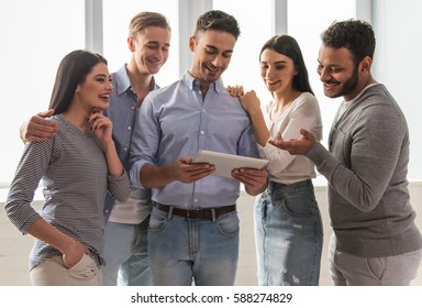 Beautiful young people in casual clothes are using a digital tablet, talking and smiling - Shutterstock ID 588274829