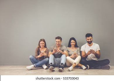 Beautiful young people are using smartphones and smiling while sitting on the floor - Powered by Shutterstock