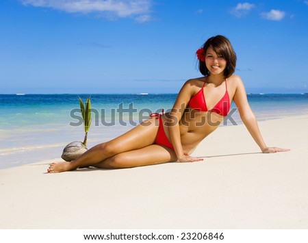 a beautiful young Polynesian girl in a red bikini on a Hawaii beach at midday with a sprouting coconut nearby on the sand