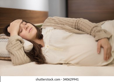 Beautiful young pregnant woman feeling head ache and laying on the bad in the room with modern furniture  - Powered by Shutterstock