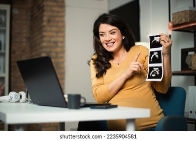 Beautiful young pregnant woman holding ultrasound pictures of her baby. Businesswoman having video call - Shutterstock ID 2235904581