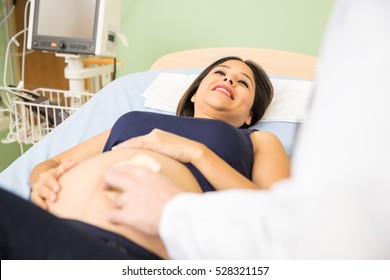 Beautiful young pregnant woman lying on a hospital bed while a doctor performs and ultrasound