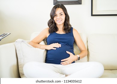 Beautiful young pregnant woman touching her belly and smiling while relaxing at home