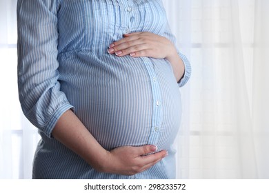 Beautiful young pregnant woman touching her belly on light background