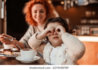 Beautiful young red-haired mother with cute curly-haired daughter are sitting in cozy cafe and drinking hot school. Mothers Day. - Powered by Shutterstock