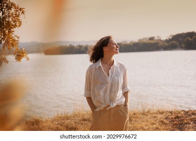 Beautiful young relaxed woman in white blouse enjoying nature breathing fresh air meditating on the river on an autumn