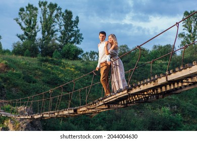 Beautiful young romantic couple standing and hugging on the suspension bridge above the river - Powered by Shutterstock