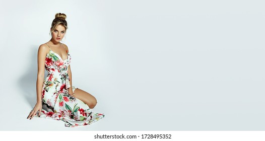 Beautiful young romantic girl in a white long dress with floral print sits in the studio on a white background.