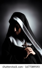 beautiful young sad nun holding cross on grey