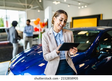 Beautiful young saleswoman working at car showroom. Customers in the background. 