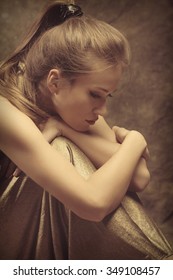 Beautiful Young Sensual Woman In Golden Dress Sit With Wrap  Arms Around Legs, Side View, Studio Shot