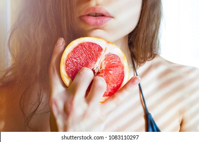 
beautiful young sexy woman in bikini holding two fingers on grapefruit 
on the background of her lips. Sex concept.