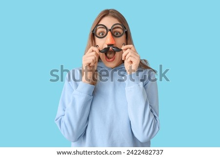 Beautiful young shocked woman in funny disguise on blue background. April Fools Day celebration