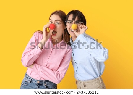 Beautiful young shocked women with funny clown noses on yellow background. April Fools Day celebration