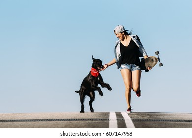 Beautiful young skater playing with her dog in the city.