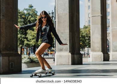 Beautiful young skater woman riding on her longboard in the city. Stylish girl in street clothes rides on a longboard.