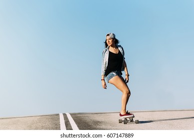 Beautiful young skater woman riding on her longboard in the city.