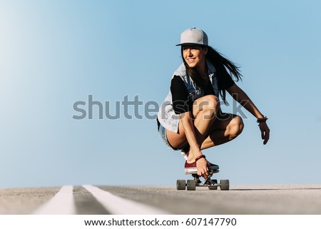 Beautiful young skater woman riding on her longboard in the city.