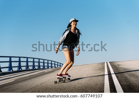 Beautiful young skater woman riding on her longboard in the city.