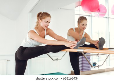Beautiful young slender woman in sportswear stretching near the ballet barre.