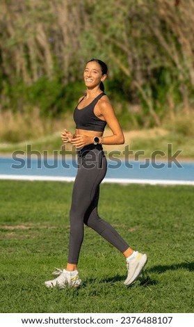 Beautiful young slim and tanned runner girl, dressed in tight sportswear, stopping from running enjoying and smiling looking at camera happy on a sunny day.