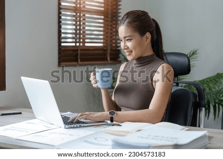 Beautiful young smiling asian woman working on laptop and drinking coffee in living room at home. Asia business woman working document finance and calculator in her home office
