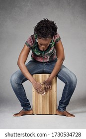 
beautiful young smiling black african woman playing music with cajon on gray isolated studio background