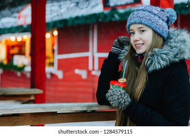 Beautiful young smiling Caucasian girl in winter clothes drinking hot mulled wine on winter fair. Concert Christmas Holidays. Outdoor, daylight. Copy space. - Shutterstock ID 1284579115