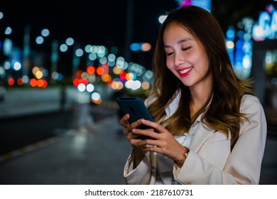 Beautiful Young Smiling Female Texting Work Message On Smartphone Outside Office, Business Woman Using Mobile Phone Walking Through Night City Street While Waiting Car To Pick Up Home, Social Media