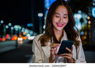 Beautiful Young Smiling Female Texting Work Message On Smartphone Outside Office, Business Woman Using Mobile Phone Walking Through Night City Street While Waiting Car To Pick Up Home, Social Media