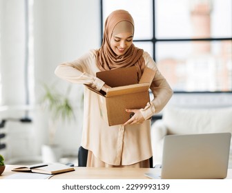 Beautiful young smiling muslim woman in traditional religious hijab   unpacking delivered order from cardboard box while at table in home office
 - Powered by Shutterstock