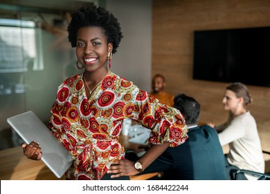 Beautiful young smiling professional black african business woman holding laptop, coworkers hold a meeting in background