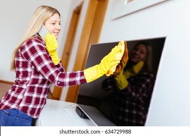 Beautiful Young Smiling Woman Cleaning House With Microfiber Cloth While Talking On Phone. 