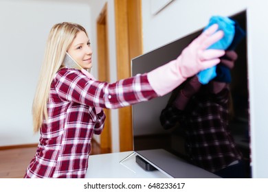 Beautiful Young Smiling Woman Cleaning House With Microfiber Cloth While Talking On Phone. 