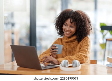 Beautiful young smiling woman with curly hair working on laptop and drinking coffee sitting at cafe. - Powered by Shutterstock