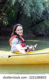 Beautiful young smiling woman paddling in yellow kayak on river. Perfect day for kayaking.