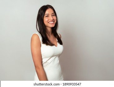 Beautiful young and smiling woman posing in dress on grey background