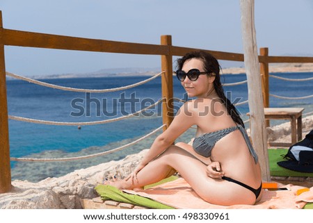 Beautiful young smiling woman sitting  on sun lounger opposite the sea with corals and reefs at exotic beach