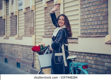 Beautiful young smiling woman walking with bicycle and waving hand on city street.  Beauty,gesture and  lifestyle concept
