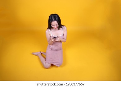 Beautiful Young South East Asian Woman Sit Down On Floor Yellow Orange Color Background Hold Use Text Smart Phone Pose Fashion Style Elegant Beauty Mood