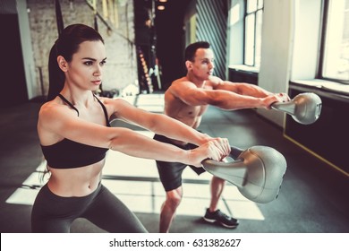 Beautiful Young Sports Couple Is Working Out With Kettlebell In Gym